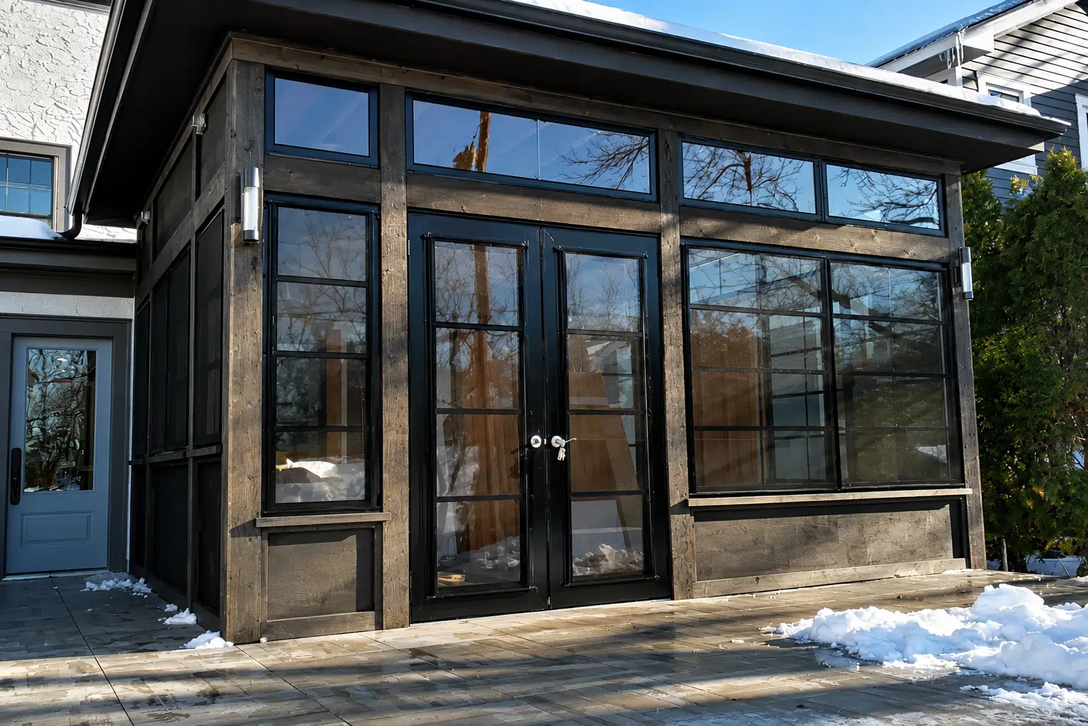 Modern black-framed double doors on a porch enclosure with glass panes and matching side windows